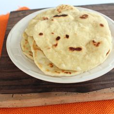 three tortillas on a white plate sitting on an orange place mat next to a wooden cutting board