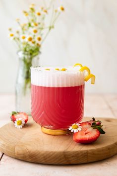 a strawberry and lemonade drink on a wooden board with flowers in the vase behind it