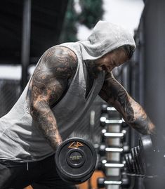 a man with tattoos is holding a barbell in front of a gym equipment rack