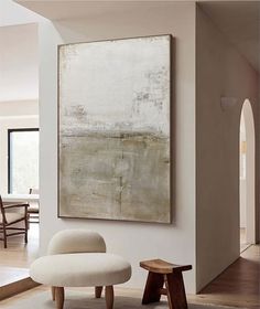 an abstract painting hangs on the wall above a chair and footstool in a living room