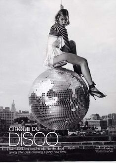 a woman sitting on top of a disco ball in front of a cityscape