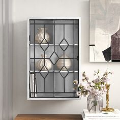 a vase with flowers on a table in front of a wall mounted bookcase that has glass doors