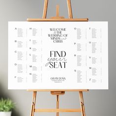 a wooden easer with a wedding seating chart on it next to a potted plant