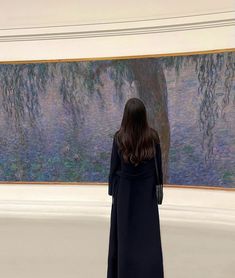 a woman standing in front of a painting looking at the ground and back to the camera