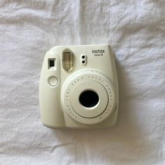 a white polaroid camera sitting on top of a bed next to a white sheet