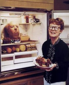 a woman holding a plate in front of an open refrigerator with food on the door