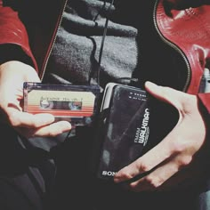 a person holding an old school cassette and cell phone in their hands, while wearing a red leather jacket