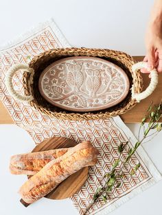 two loaves of bread sitting in a bowl on a cutting board next to some herbs