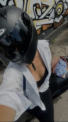 a woman in white shirt and black helmet sitting next to a wall with graffiti on it