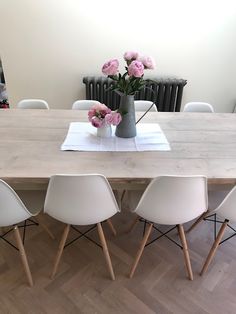 a wooden table with white chairs and pink flowers in a vase on the center piece