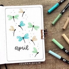 an open notebook with the word april written on it, surrounded by markers and pens