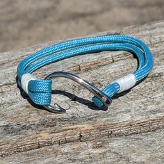 a blue and white rope bracelet on top of a piece of wood with a metal hook