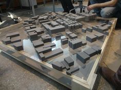 two men sitting on the floor looking at a model of a city with buildings in it