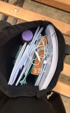 an open black bag filled with ear buds and headphones sitting on top of a wooden bench