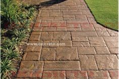 a brick walkway with grass and bushes in the background