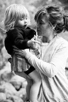 a woman holding a small child in her arms while standing next to rocks and trees