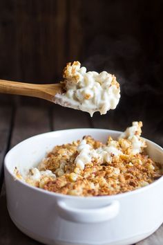 a white bowl filled with food on top of a wooden table next to a spoon