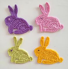 three crocheted rabbits sitting next to each other on a white surface with yellow, pink, and purple colors