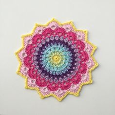 a crocheted doily is shown on a white surface with pink, yellow and blue colors