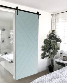 a bedroom with a bed, plant and sliding glass door that opens to the bathroom