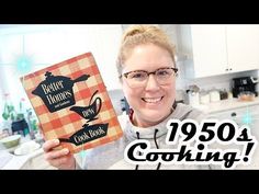 a woman holding up a cook book in her kitchen with the title, 1950 cooking