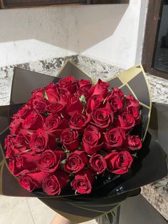 a bouquet of red roses sitting on top of a black box with gold foil around it