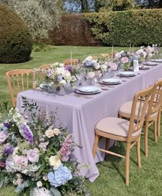 a long table with purple and white flowers is set up for an outdoor dinner party