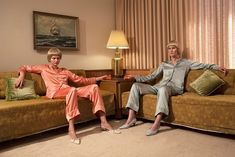 two women sitting on couches in a living room with lamps and paintings behind them