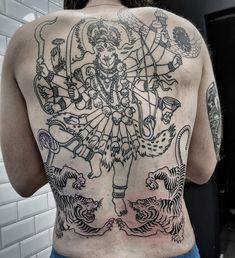 the back of a woman's body with tattoos on it and an image of a demon