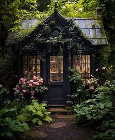 a small black house surrounded by greenery and flowers in front of a door with windows