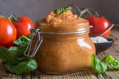 a jar filled with food sitting on top of a wooden table next to tomatoes and basil