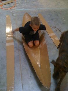 a young boy riding on top of a wooden boat next to a brown dog in a room