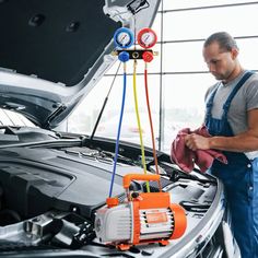 a man in overalls working on the hood of a car with an air conditioner