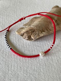 a red and black beaded necklace on a piece of wood with a white pearl