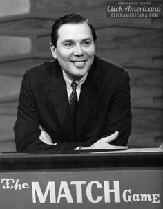 a black and white photo of a man sitting in front of a match game sign