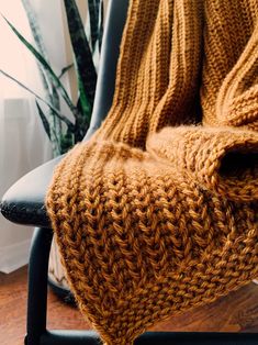 a chair with a knitted blanket on it in front of a potted plant