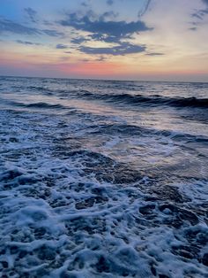 the sun is setting over the ocean with waves crashing on the shore and clouds in the sky