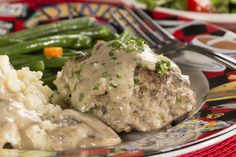 a plate topped with meat covered in gravy next to mashed potatoes and green beans