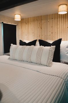 a bed with white and black pillows in a bedroom next to wooden wall paneling