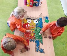 three children in orange shirts are making a paper cut out of a cat on a table