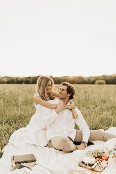 a man and woman sitting on top of a blanket in the middle of a field