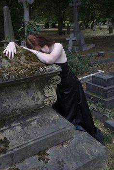 a woman in black dress leaning over a grave