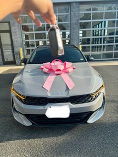 a car with a pink ribbon tied to it's hood is parked in front of a building