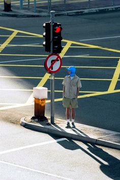 a man wearing a blue hat standing next to a traffic light on the side of a road