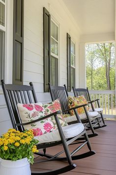 three rocking chairs on the front porch with pillows and flowers in vases next to them