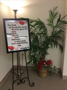 a sign in front of a potted plant with flowers on it that says for god so loved the world