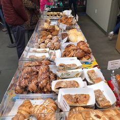 many different types of pastries are on display at the buffet table with people standing around