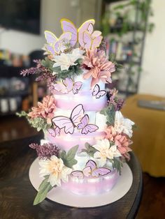 a three tiered cake with flowers and butterflies on the top, sitting on a table