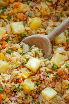 rice and vegetables are mixed together in a skillet with a wooden spoon on the side