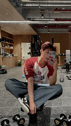 a young man sitting on the ground taking a selfie with his cell phone while surrounded by dumbbells